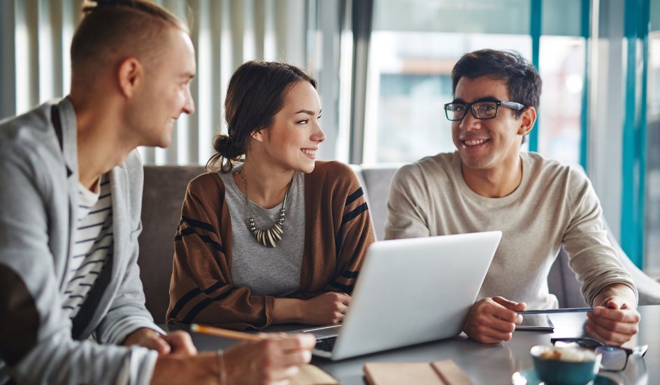 group sitting at table looking at a laptop communicating