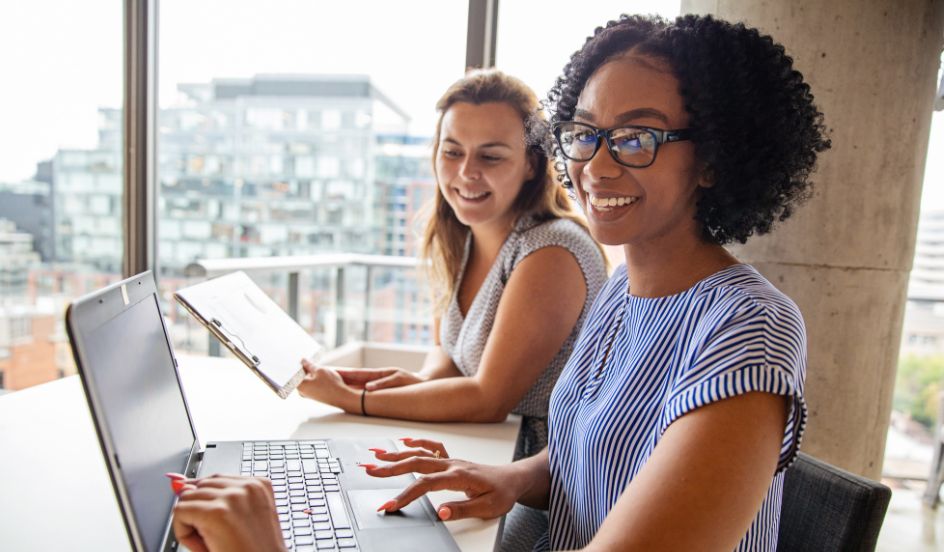 woman smiling while working with co-worker while on laptop