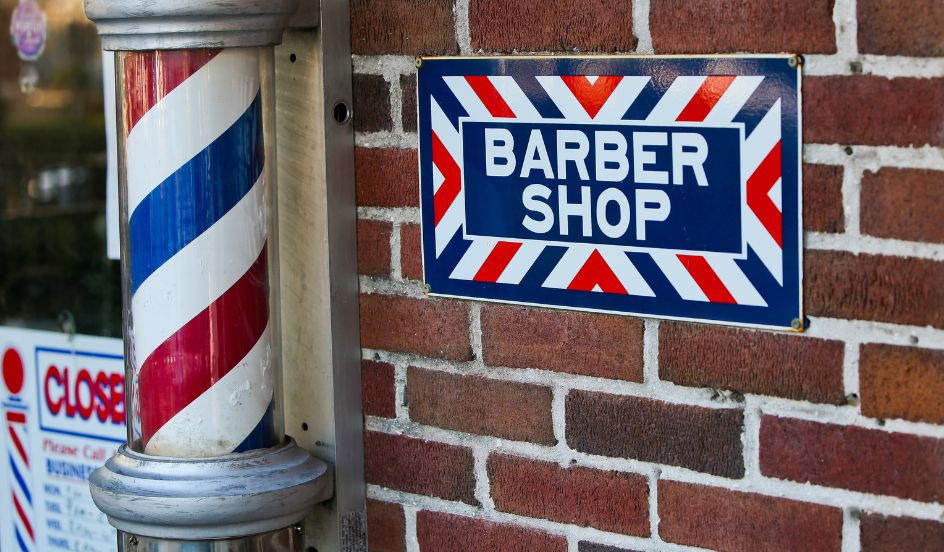 old fashioned red white and blue barber pole with barber sign on brick wall