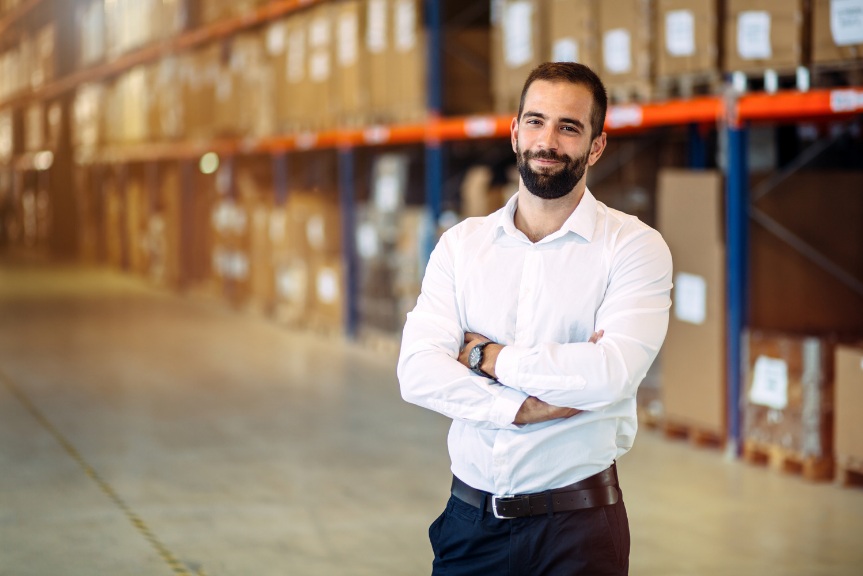 A logistics and supply chain manager stands inside a warehouse.