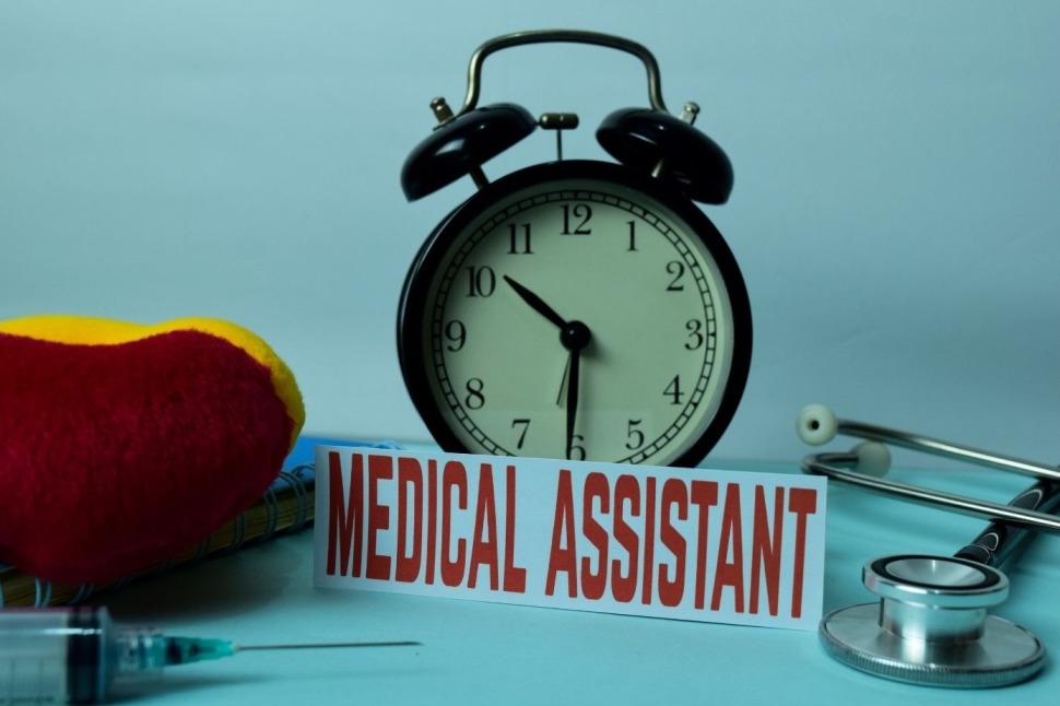 Medical assistant sign against an alarm clock on a table