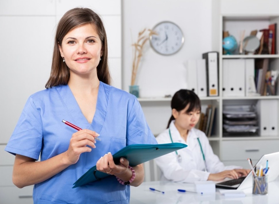 Medical office assistant standing in front of a working doctor