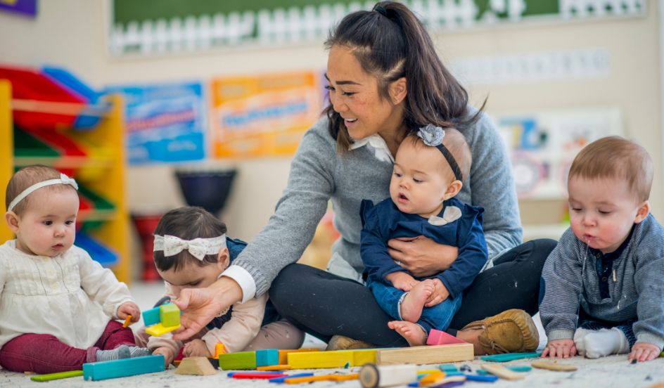 ECE engaging with infants playing with blocks on floor