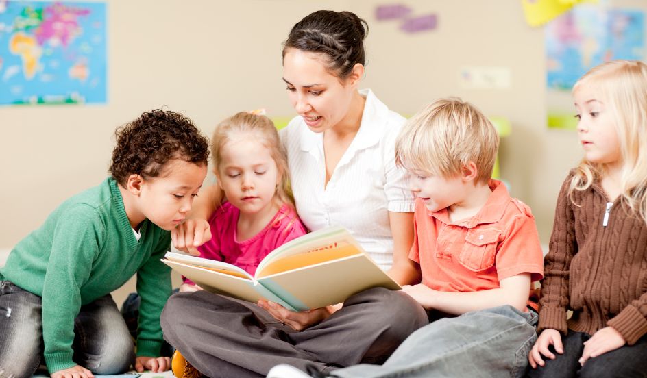 ECE reading a book sitting on the floor with young children