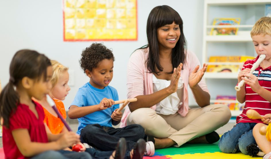 ECE teaching music with instruments with young children sitting on floor