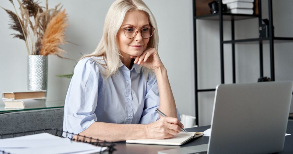 Woman taking notes for her online classes while watching her computer monitor.